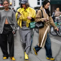 Drei Frauen in modischen Outfits, die die Herbstfarbe Gelb und Grau tragen, spazieren durch die Stadt.