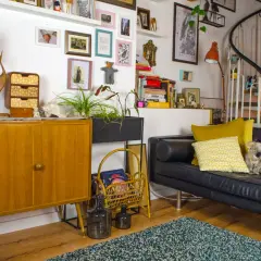 Gemütliche hygge einrichtung mit Vintage-Möbeln, Kunst und Pflanzen. Ein schwarzes Ledersofa lädt zum Entspannen ein.