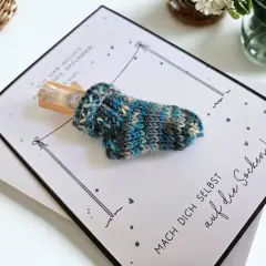 Gestrickte Socke mit Geld als Geschenk. Die Karte fragt "wie viele Socken braucht man?" und ermutigt, sich selbst auf die Socken zu machen.