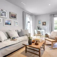 Gemütliches Wohnzimmer mit einem großen Sofa, einem Holztisch und einem Schaukelstuhl. Die warmes grau farbpalette schafft eine beruhigende Atmosphäre.