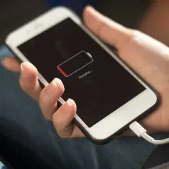 Hand hält Smartphone mit leerem Akku, das gerade geladen wird. Die Frage "wie lange handy nutzen" stellt sich, wenn der Akku fast leer ist.