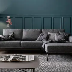Gemütliche graue Couch mit vielen Kissen auf einem gemusterten Teppich. Ein moderner Couchtisch mit Buch steht davor.