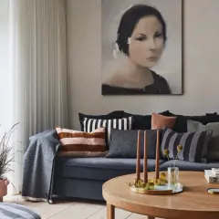 Gemütliches, warmes Wohnzimmer mit einem Sofa voller Kissen, einem Gemälde und einem Holztisch mit Kerzen.