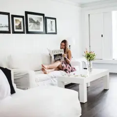 Frau liest Magazin auf weißem Sofa, umgeben von minimalistisch eingerichteten Räumen. Helle Farben und klare Linien schaffen eine ruhige Atmosphäre.