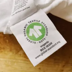 GOTS-zertifiziertes Textiletikett auf weißem Stoff. Die Kritik an der Textilindustrie wird durch das Siegel "Global Organic Textile Standard" entkräftet.