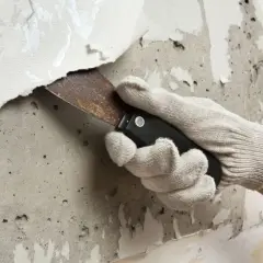 Mit einem Spachtel wird eine alte Tapete von der Wand entfernt. Die Arbeit, um die Fototapete zu entfernen, ist mühsam.