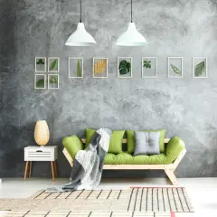 Graue Beton-Struktur Wand mit gerahmten Blättern und einem grünen Sofa.
