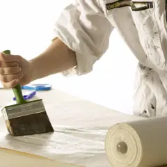 Hand mit Kleisterbürste auf glatter Raufasertapete, bereit für die Wand.