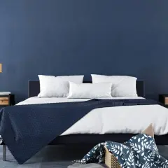 Ein modernes Schlafzimmer mit tiefblauen Wänden, die zum Streichen in Blau einladen. Ein dunkles Bett mit weißen Kissen und einer blauen Decke.