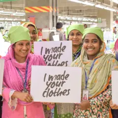 Frauen in einer Fabrik halten Schilder mit "I made your clothes". Dies unterstreicht die Bedeutung der Fair Wear Foundation für faire Arbeitsbedingungen.
