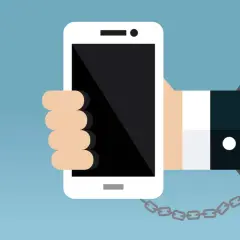 Eine Hand hält ein Smartphone, das mit einer Handschelle und Kette gefesselt ist. Ein Symbol für zu viel Handy-Nutzung.