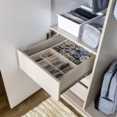 Schrank mit ordentlich gefalteten Kleidungsstücken in Schubladen und Körben. Ein Rucksack und Jeans hängen daneben. Zu viele Klamotten zu wenig Platz? Hier ist die Lösung!