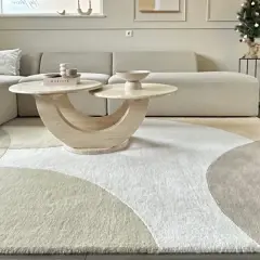 Ein Wohnzimmer mit einem beigen Ecksofa, einem runden Couchtisch und einem modernen Teppich im geometrischen Design. Dieser Teppich-Trend bringt Ruhe und Stil in jeden Raum.