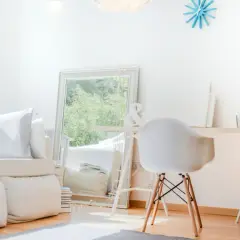 Ein helles, aufgeräumtes Wohnzimmer mit weißem Sofa, Spiegel und Schreibtisch. Perfekt, um das **Zimmer auszumisten** und Ordnung zu schaffen.