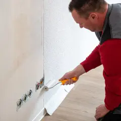 Mann tapeziert eine Wand. Der Kleisterroller wird auf den Putz aufgetragen, bevor die Tapete angebracht wird.