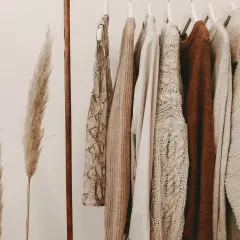 Kleidung in Erdtönen an einer Kleiderstange. Ein Statement gegen Fast Fashion: Qualität statt Quantität.