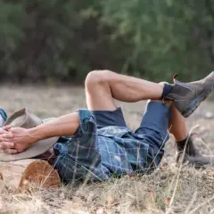Mann liegt entspannt im Gras, Hut auf dem Gesicht. Ausmisten befreit – er genießt die Ruhe nach getaner Arbeit.