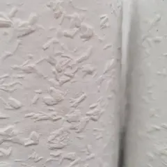 Nahaufnahme einer weißen Wand mit Raufaserputz innen. Die Struktur ist unregelmäßig und rustikal, perfekt für ein gemütliches Zuhause.