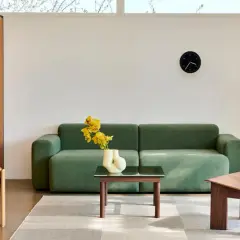 Ein Wohnzimmer im **Scandi Style** mit einem grünen Sofa, einem Holzsessel, einem Beistelltisch mit Lampe und einem Couchtisch mit gelben Blumen.