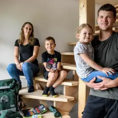 Familie auf Treppe, bereit für die Einschulung. Der Vater hält die Tochter, der Sohn sitzt daneben. Schulranzen und Mäppchen sind schon da.