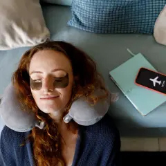 Frau mit Augenmaske und Nackenkissen entspannt sich, bereit, das handy weglegen und zu schlafen.