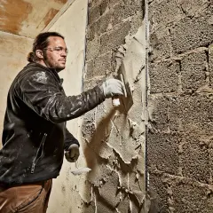 Mann verputzt eine grobe Ziegelwand mit einer Kelle. Der Putz wird gleichmäßig aufgetragen, um die Oberfläche zu glätten.