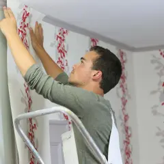 Mann bringt fototapete auf raufaser an. Rote Blumenmuster zieren die Wand.