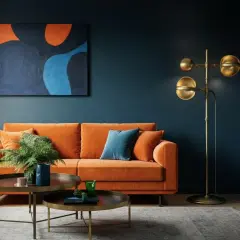 Ein orangefarbenes Sofa vor einer dunkelblauen Wand. Die Frage, welche Farbe passt zu blau Wandfarbe, wird hier mit einem kräftigen Orange beantwortet.
