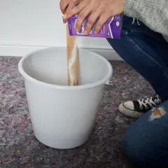 Hände schütten Pulver aus einer Packung in einen Eimer, um Tapetenkleister aufzutragen.