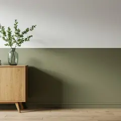 Ein Sideboard aus Holz mit Büchern und einer Vase mit Zweigen steht vor einer zweifarbig gestrichenen Wand. Die untere Hälfte der Wand ist in einem erdigen Grün gehalten, die obere Hälfte in Weiß.
