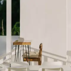Ein Holztisch mit einer Box, ein Stuhl mit Kissen und weiße Möbel auf einer Terrasse. Hier lässt es sich schlicht und einfach leben.