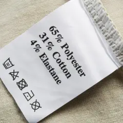 Pflegeetikett mit Materialzusammensetzung: 65% Polyester, 31% Baumwolle, 4% Elastan. Die Textilkette ist gut lesbar.