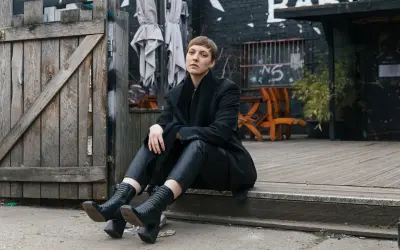 Frau in schwarzem Outfit sitzt vor Holztür. Sie überlegt, wieviel spart man wenn man keine kleidung mehr kaufen muss.