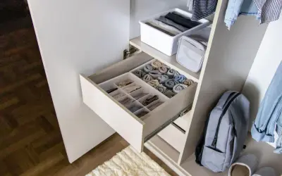 Schrank mit ordentlich gefalteten Kleidungsstücken in Schubladen und Körben. Ein Rucksack und Jeans hängen daneben. Zu viele Klamotten zu wenig Platz? Hier ist die Lösung!