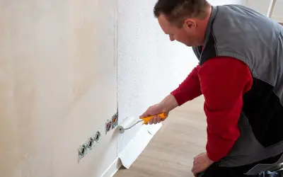 Mann tapeziert eine Wand. Der Kleisterroller wird auf den Putz aufgetragen, bevor die Tapete angebracht wird.