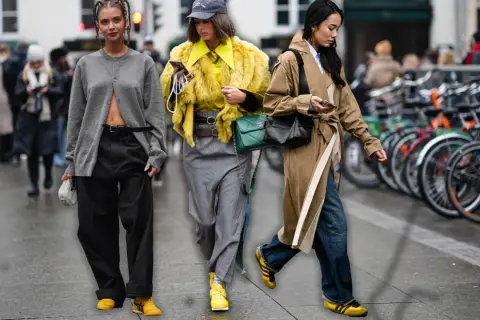 Drei Frauen in modischen Outfits, die die Herbstfarbe Gelb und Grau tragen, spazieren durch die Stadt.