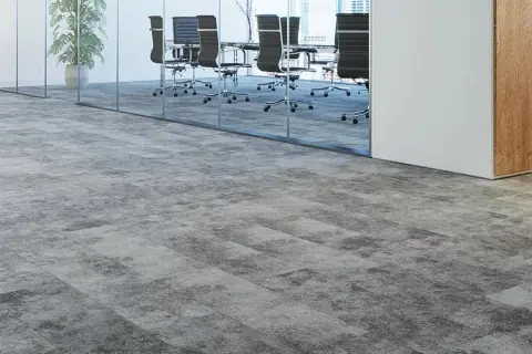 Moderner Teppichboden in Grau auf grauen Fliesen, der einen stilvollen Übergang zu einem Konferenzraum mit Glaswänden und Bürostühlen schafft.