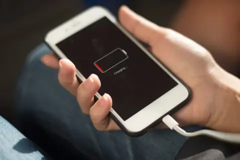Hand hält Smartphone mit leerem Akku, das gerade geladen wird. Die Frage "wie lange handy nutzen" stellt sich, wenn der Akku fast leer ist.