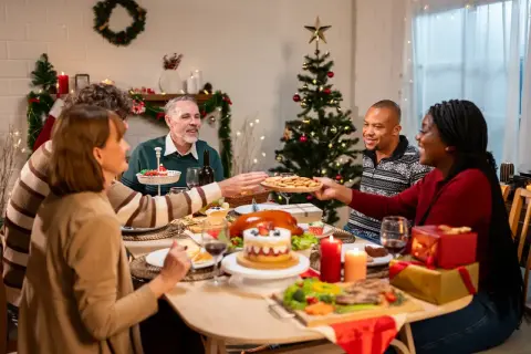 Familie feiert Weihnachten minimalistisch am festlich gedeckten Tisch. Ein Weihnachtsbaum und Kerzen sorgen für stimmungsvolles Licht.