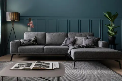 Gemütliche graue Couch mit vielen Kissen auf einem gemusterten Teppich. Ein moderner Couchtisch mit Buch steht davor.