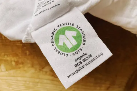 GOTS-zertifiziertes Textiletikett auf weißem Stoff. Die Kritik an der Textilindustrie wird durch das Siegel "Global Organic Textile Standard" entkräftet.
