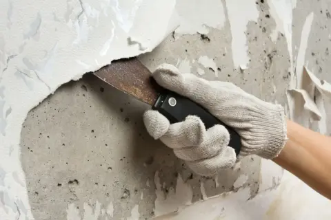 Mit einem Spachtel wird eine alte Tapete von der Wand entfernt. Die Arbeit, um die Fototapete zu entfernen, ist mühsam.