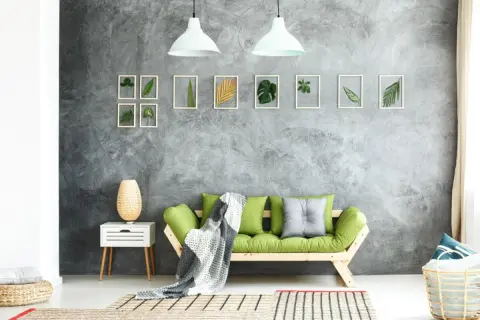 Graue Beton-Struktur Wand mit gerahmten Blättern und einem grünen Sofa.