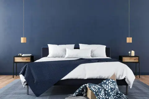 Ein modernes Schlafzimmer mit tiefblauen Wänden, die zum Streichen in Blau einladen. Ein dunkles Bett mit weißen Kissen und einer blauen Decke.