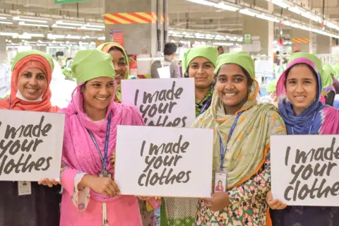 Frauen in einer Fabrik halten Schilder mit "I made your clothes". Dies unterstreicht die Bedeutung der Fair Wear Foundation für faire Arbeitsbedingungen.
