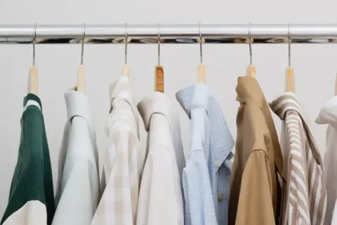 Eine Auswahl an Hemden und einem grünen Pullover für einen stilvollen **capsule wardrobe mann**.