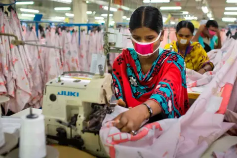 Frauen mit Masken arbeiten an Nähmaschinen. Sie sind Teil einer nachhaltigen Textilproduktion, die auf faire Arbeitsbedingungen und umweltfreundliche Prozesse setzt.