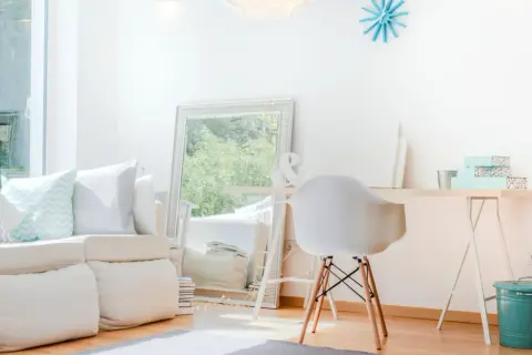 Ein helles, aufgeräumtes Wohnzimmer mit weißem Sofa, Spiegel und Schreibtisch. Perfekt, um das **Zimmer auszumisten** und Ordnung zu schaffen.