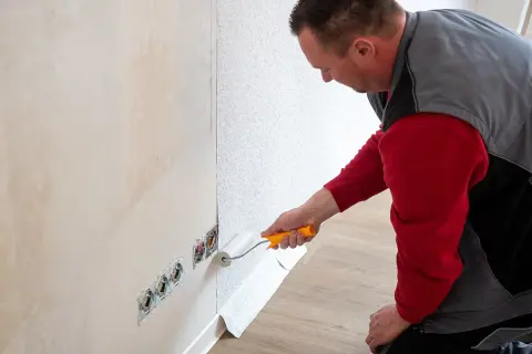 Mann tapeziert eine Wand. Der Kleisterroller wird auf den Putz aufgetragen, bevor die Tapete angebracht wird.