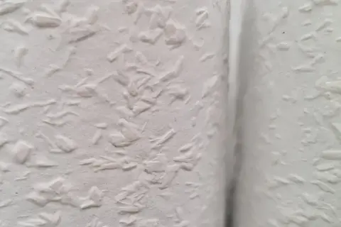 Nahaufnahme einer weißen Wand mit Raufaserputz innen. Die Struktur ist unregelmäßig und rustikal, perfekt für ein gemütliches Zuhause.